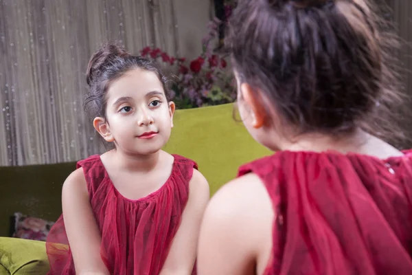 Small beautiful arab middle eastern girl with pretty red dress and lips posing and looking at herself in mirror. 8-10 years. — Stock Photo, Image