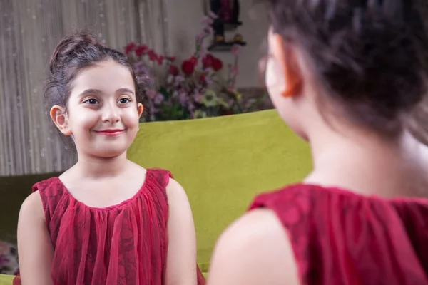 Small beautiful arab middle eastern girl with pretty red dress and lips posing and looking at herself in mirror. 8-10 years. — Stock Photo, Image