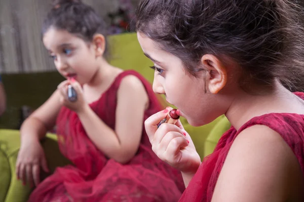 Micuță fată frumoasă arabă din Orientul Mijlociu cu rochie și buze destul de roșii care se machiază cu atenție acasă în oglindă. 8-10 ani . — Fotografie, imagine de stoc