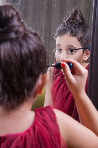 Pequeña hermosa chica árabe del medio oriente con bonito vestido rojo y labios haciendo maquillaje cuidadosamente en casa en el espejo. 8-10 años . — Foto de Stock