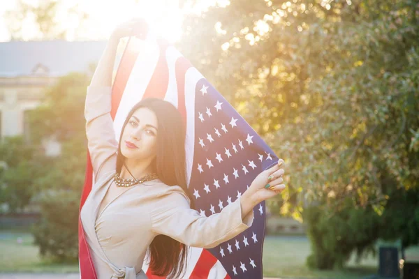 Piękna młoda kobieta z klasyczna sukienka gospodarstwa amerykańską flagę w parku. modelka trzyma nas uśmiechając się i patrząc na kamery. USA styl życia. — Zdjęcie stockowe