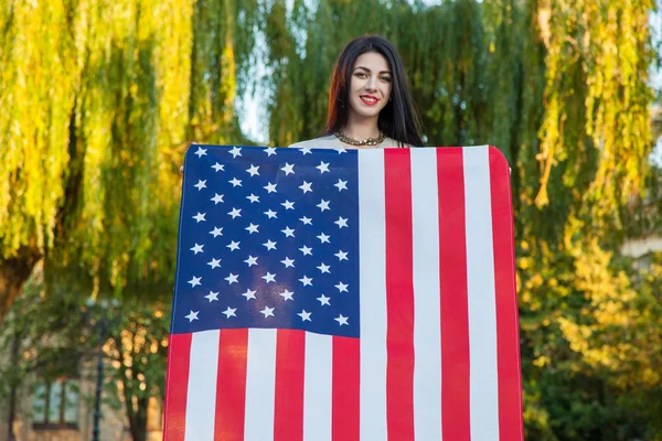 Beautiful young woman with classic dress holding american flag in the park. fashion model holding us smiling and looking at camera. usa lifestyle. — Stock Photo, Image