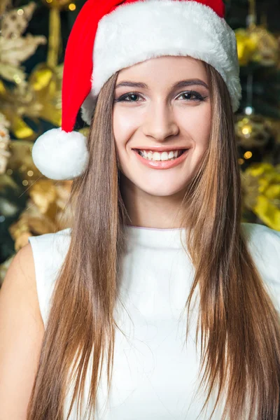 Jovem engraçado modelo de moda bonita com olhos escuros, cabelo castanho e chapéu de Papai Noel celebrando o ano novo em casa. decoração do ano novo, com emoção positiva posando e olhando para a câmera. decoração de ouro amarelo — Fotografia de Stock