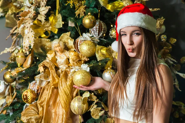 Jovem engraçado modelo de moda bonita com olhos escuros, cabelo castanho e chapéu de Papai Noel celebrando o ano novo em casa. decoração do ano novo, com emoção positiva posando e olhando para a câmera. decoração de ouro amarelo — Fotografia de Stock