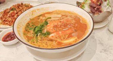 İçinde baharatlı, lezzetli bir şehriye çorbası olan büyük beyaz bir kase, muhtemelen Laksa veya Tom Yum gibi bir Güneydoğu Asya yemeği. 