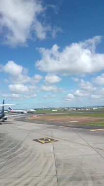 Malezya, Kuala Lumpur 01.01.2025 uçak penceresinden havalimanı pistinin dikey portre görüntüsü, bulutlu gökyüzü, taksi işaretleri ve KLIA 'dan kalkan hareket halindeki yer araçları ve hava araçları