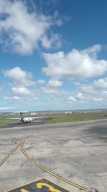 Malezya, Kuala Lumpur 01.01.2025 uçak penceresinden havalimanı pistinin dikey portre görüntüsü, bulutlu gökyüzü, taksi işaretleri ve KLIA 'dan kalkan hareket halindeki yer araçları ve hava araçları