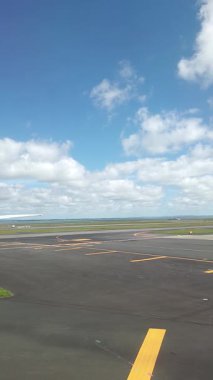 Malezya, Kuala Lumpur 01.01.2025 uçak penceresinden havalimanı pistinin dikey portre görüntüsü, bulutlu gökyüzü, taksi işaretleri ve KLIA 'dan kalkan hareket halindeki yer araçları ve hava araçları