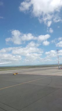 Malezya, Kuala Lumpur 01.01.2025 uçak penceresinden havalimanı pistinin dikey portre görüntüsü, bulutlu gökyüzü, taksi işaretleri ve KLIA 'dan kalkan hareket halindeki yer araçları ve hava araçları