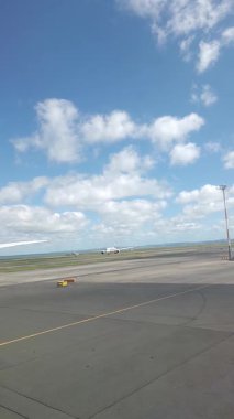 Malezya, Kuala Lumpur 01.01.2025 uçak penceresinden havalimanı pistinin dikey portre görüntüsü, bulutlu gökyüzü, taksi işaretleri ve KLIA 'dan kalkan hareket halindeki yer araçları ve hava araçları