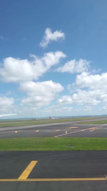 Malezya, Kuala Lumpur 01.01.2025 uçak penceresinden havalimanı pistinin dikey portre görüntüsü, bulutlu gökyüzü, taksi işaretleri ve KLIA 'dan kalkan hareket halindeki yer araçları ve hava araçları