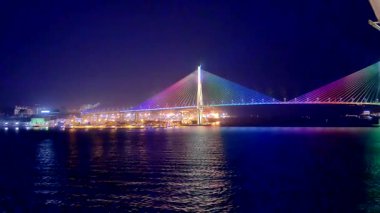 Busan, Güney Kore, 1 Ocak 2025, Busan, Güney Kore 'de bir asma kablo köprüsünün gece görüntüsü, gökkuşağı ışıklarıyla güzelce aydınlatılmış, suya ve deniz yolculuğundan gelen tekneye yansıyan.