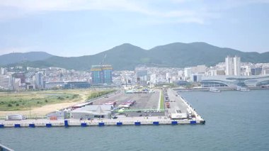 Kore, 1 Ocak 2025, geniş bir çekim Busan Limanı 'na yaklaşan büyük bir yolcu gemisi gösteriyor, sakin suları, liman tesisleri ve Busan, Güney ufuk çizgisi 