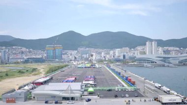 Kore, 1 Ocak 2025, geniş bir çekim Busan Limanı 'na yaklaşan büyük bir yolcu gemisi gösteriyor, sakin suları, liman tesisleri ve Busan, Güney ufuk çizgisi 