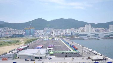 Kore, 1 Ocak 2025, geniş bir çekim Busan Limanı 'na yaklaşan büyük bir yolcu gemisi gösteriyor, sakin suları, liman tesisleri ve Busan, Güney ufuk çizgisi 