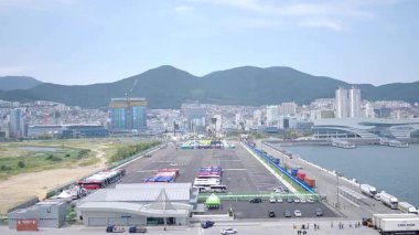 Kore, 1 Ocak 2025, geniş bir çekim Busan Limanı 'na yaklaşan büyük bir yolcu gemisi gösteriyor, sakin suları, liman tesisleri ve Busan, Güney ufuk çizgisi 