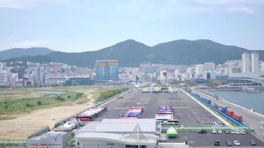 Kore, 1 Ocak 2025, geniş bir çekim Busan Limanı 'na yaklaşan büyük bir yolcu gemisi gösteriyor, sakin suları, liman tesisleri ve Busan, Güney ufuk çizgisi 