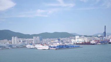 Busan, Güney Kore, 1 Ocak 2025 Geniş açılı çekimde Kore 'deki Busan limanına yaklaşan bir yolcu gemisi görülüyor. Kıyı kenti binaları, vinçler ve liman tesisleri görünüyor. 