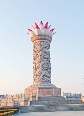 Shaanxi, Çin, 1 Ocak 2026, Bulut ve su tarzında karmaşık ejderha rahatlamaları içeren muazzam bir taş sütun, çiçek açan beyaz ve pembe nilüfer ile kaplı