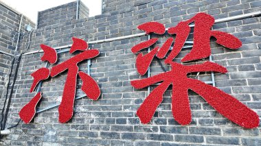 KaiFeng, Çin, 1 Ocak 2026, büyük kırmızı Çin karakterleri gri tuğla duvara asılmış, tarihi kale duvarlarına karşı cesur bir kültürel tabela oluşturuyorlar.