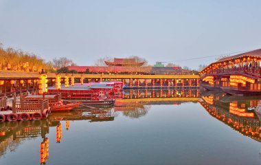 KaiFeng, Çin, 1 Ocak 2026, geleneksel Çin şehrinde panoramik nehir sahnesi, kırmızı botlar, ahşap pavyonlar, durgun su ve temiz gökyüzü altında tarihi binalar.
