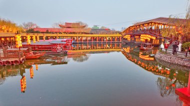 KaiFeng, Çin, 1 Ocak 2026, geleneksel Çin şehrinde panoramik nehir sahnesi, kırmızı botlar, ahşap pavyonlar, durgun su ve temiz gökyüzü altında tarihi binalar.