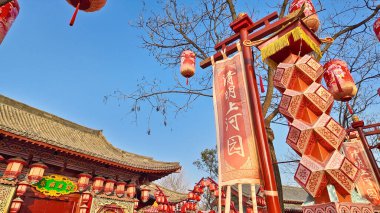 Tepemizde asılı parlak kırmızı Çin fenerlerinden oluşan yoğun bir küme açık mavi gökyüzüne karşı dramatik bir gölgelik oluşturuyor.