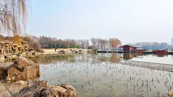 Sakin suları, çıplak kış ağaçları, yürüyüş yolları, küçük köprüler ve berrak gökyüzü altında sakin manzaralı atmosferi olan huzurlu göl parkı.