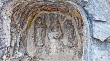 Eski Budist taş heykeli Longmen mağarası içinde, solgun duvar resimleri ve tapınağın etrafını saran karmaşık kaya dokularıyla Buda oyulmuş.