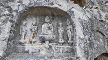 Eski Budist taş heykeli Longmen mağarası içinde, solgun duvar resimleri ve tapınağın etrafını saran karmaşık kaya dokularıyla Buda oyulmuş.