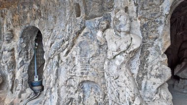 Eski Budist taş heykeli Longmen mağarası içinde, solgun duvar resimleri ve tapınağın etrafını saran karmaşık kaya dokularıyla Buda oyulmuş.