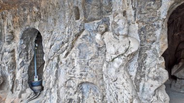 Eski Budist taş heykeli Longmen mağarası içinde, solgun duvar resimleri ve tapınağın etrafını saran karmaşık kaya dokularıyla Buda oyulmuş.