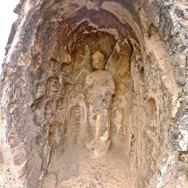 Eski Budist taş heykeli Longmen mağarası içinde, solgun duvar resimleri ve tapınağın etrafını saran karmaşık kaya dokularıyla Buda oyulmuş.