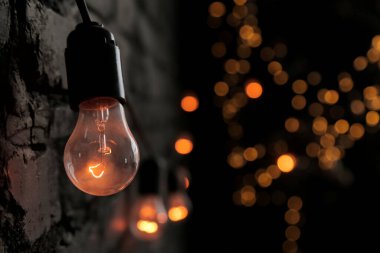 Tavan arasında koyu tuğlalı bir duvara dayanmış bir ampul güzel bir turuncu ışıkla parlıyor. Bokeh.