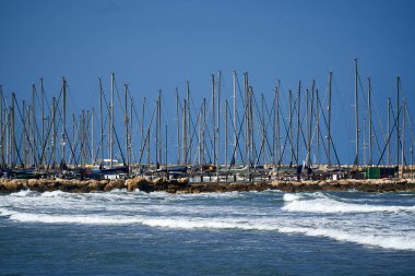                                Güneşli bir günde mavi arka planda yelkenli gemi direklerinin yatay görüntüsü ve önünde deniz dalgaları. Fotoğraf bir Tel-Aviv limanında çekildi..