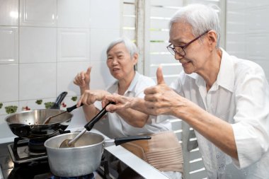Happy smiling asian senior women thumb up while cooking vegetables clear soup,elderly siblings enjoying preparing meal Thai food in kitchen at house,healthy food,concoction,family lifestyle concept clipart
