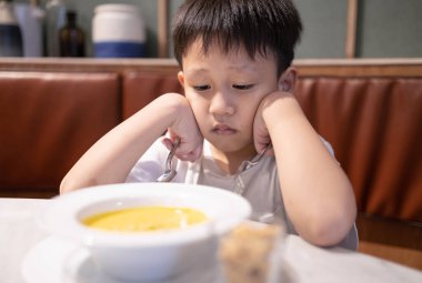 Depresyondaki iştahsız Asyalı çocuk, iştahsız, çocuk yuvası yemekten ve sıkıntıdan sıkılmış, sebze çorbası içmeyi reddeden, tatsız, yemekten, beslenmekten ve yeme bozukluğundan bıkmış çocuk yuvası.