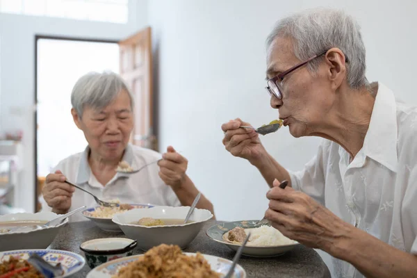 Happy asian senior women eating Thai food,local cuisine,sitting at dining table in the house,old people are enjoying lunch,eat with rice,healthy food,elderly have a good appetite,health care concept