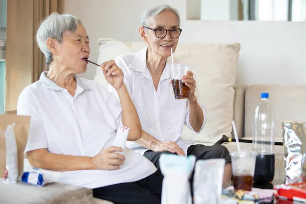 노인이 음료를 마시고 정크푸드를 집에서는 음료수 스낵을 먹으며 습관의 개념으로 — 스톡 사진