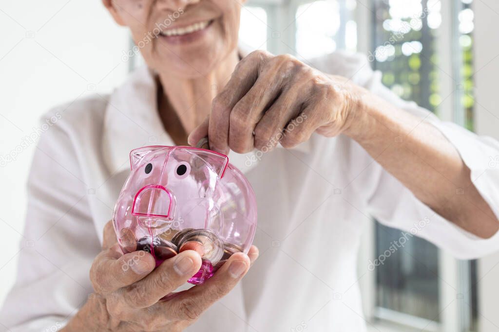 Hand of senior woman putting coins into piggy bank,Smiling elderly holding a piggy bank pink pig feel happy,saving money for health care,medical insurance,concept of financial planning in retirement