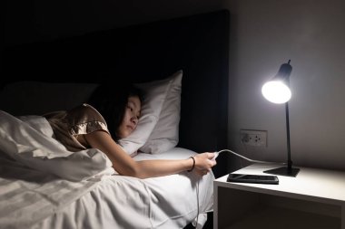 Asyalı çocuk yatakta dinleniyor, yatmadan önce ışığı kapatıyor yatak odasında uyumak için, kullanımda değilken ışıkları kapatıyor, lambayı kapatıyor, enerji tasarrufu yapıyor, tasarruf ediyor.