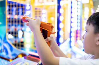 Asyalı küçük çocuk atış oyunu oynuyor, alışveriş merkezini ziyaret ederken oyuncaklarla oyun oynuyor, elinde oyuncak tabanca tutan mutlu çocuk, hedefi hedef alıyor ve eğleniyor.