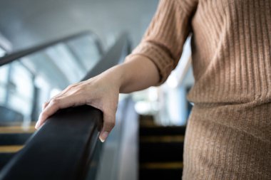 Hand of young woman touching the escalator during Coronavirus pandemic,risk of contagious or contamination of COVID-19,virus,bacteria or germs avoid touching handrail of escalator in public places clipart