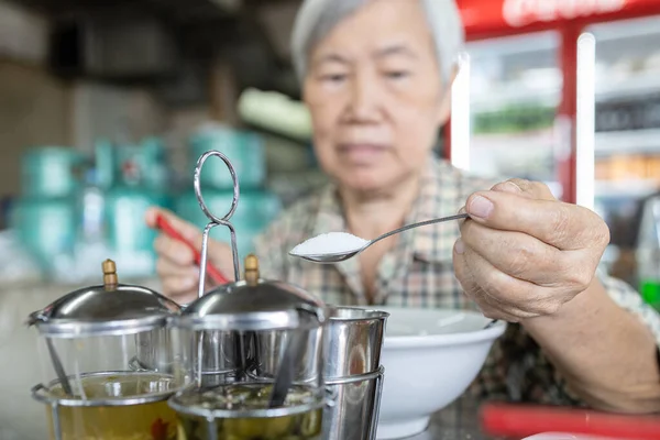 亚洲老妇人用勺子把白糖倒进她的碗里 增加食物的味道 吃太多的糖或甜味 吃太多的伤害 不健康的营养 肥胖的概念 糖尿病 — 图库照片