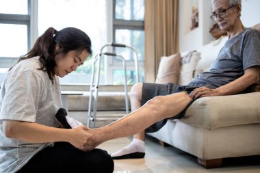 Asyalı kız yaşlılara yardım ediyor, kadın kıdemli annesinin ayaklarına çorap giyiyor, ayak parmakları uyuşmuş yaşlı insanlar, soğuğa karşı duyarsızlar, ısınmak için çorap giyiyorlar, evde sağlık hizmeti veriyorlar.