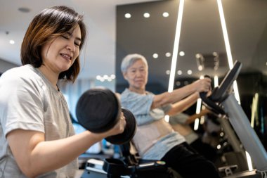 Halterle çalışan Asyalı kadın, ağırlık kaldırarak fiziksel egzersiz, bisiklet üzerinde oturan yaşlı kadın, birlikte egzersiz, spor salonunda günlük egzersiz, sağlıklı yaşam tarzı, sağlık konsepti