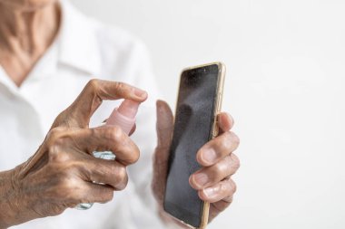 Üst düzey bir kadın cep telefonuna alkol, dezenfektan spreyi sıkarak COVID-19 enfeksiyonunu önlüyor. Mikrop bulaşmasını, bakterileri, temizleme telefonunu, Coronavirus salgınını önlüyor.