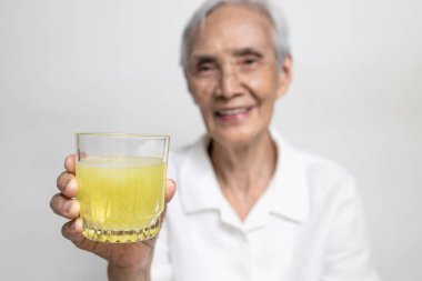 Sağlıklı Asyalı büyük anne bir bardak C vitamini ya da portakal suyu içiyor, C vitamini almış yaşlı insanlar, soğuk algınlığına karşı bağışıklığı güçlendiriyor, grip, Coronavirus 'e karşı mücadele, COVID-19