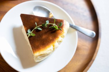 Lezzetli Bask Burnt Cheesecake, Tarta de Queso ya da San Sebastian Cheesecake beyaz seramik tabakta bir parça dilimlenmiş kaşıkla ahşap tepsiye, krema ve yumuşak peynirden yapılmış tatlı pastası