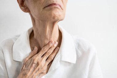 Asyalı kıdemli bir hasta eliyle boynuna dokunuyor, yaşlı yaşlının boğazı ağrıyor, yabancı bir beden boğazda sıkışmış, yutkunma ağrısı, öksürük, gırtlak iltihabı, boğaz sorunları veya gırtlak iltihabı var.